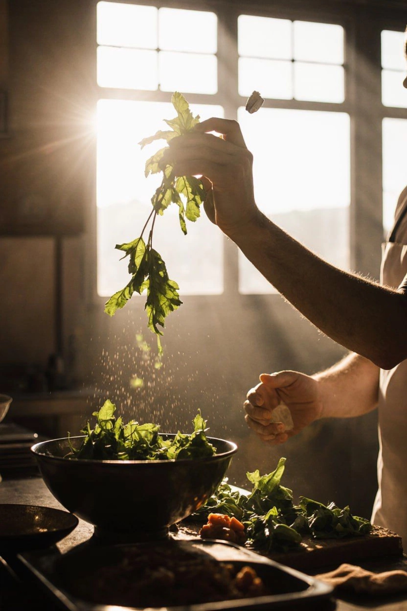 Hands sprinkling fresh herbs over a bowl in a sunlit kitchen